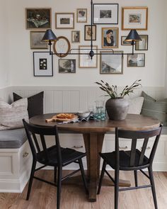 a dining room table with two chairs and pictures on the wall above it, in front of a bench