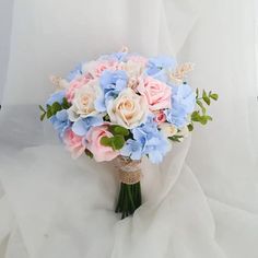 a bridal bouquet with pink, blue and white flowers on a white cloth background