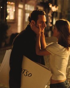 a man and woman standing next to each other holding shopping bags in their hands while looking at each other