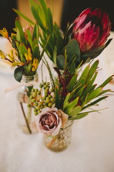 two vases filled with flowers sitting on top of a white tablecloth covered table