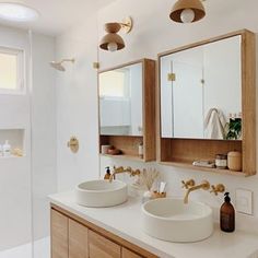 two sinks in a bathroom with wooden cabinets and mirrors above them are gold faucets