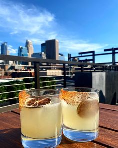 two glasses filled with drinks sitting on top of a wooden table next to each other