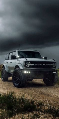 a white truck parked on top of a dirt road under a dark sky with clouds