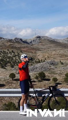 a man standing next to a bike on the side of a road with mountains in the background