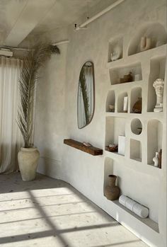 a white room with shelves, mirrors and vases on the wall next to a window