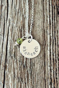 a silver necklace with a small green bead hanging from it's side on a wooden surface