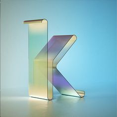 the letter k is made up of glass and has an iridescent color scheme