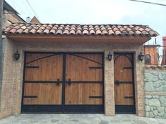 two wooden garage doors are open in front of a brick building with stone walls and tiled roof