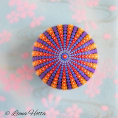 an orange and purple beaded brooch sitting on top of a blue table cloth