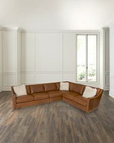 a large brown leather sectional sofa in an empty room with wood flooring and white walls