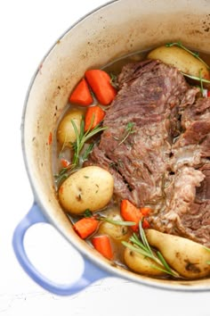 pot roast with carrots, potatoes and rosemary in a blue pan on a white surface