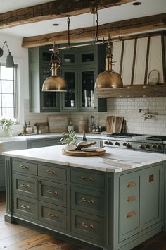 a kitchen with green cabinets and white marble counter tops, gold pendant lights over the island