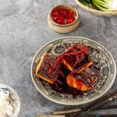 a plate with some food on it next to chopsticks and bowls filled with rice