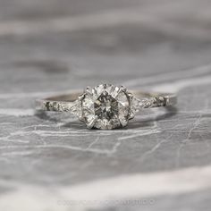 an old - fashioned diamond engagement ring sits on a marble surface