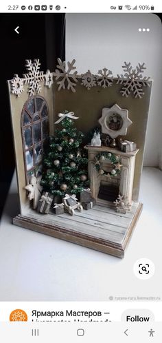 a small christmas tree is in front of a miniature house with snowflakes on the windowsill