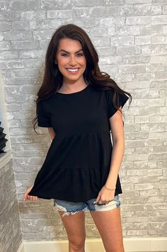 a woman standing in front of a brick wall with her hands on her hips and smiling at the camera