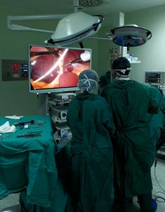 two doctors in scrubs are watching the tv screen while another surgeon is operating on it