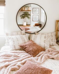 a bedroom with a round mirror on the wall and pillows on the bed in front of it