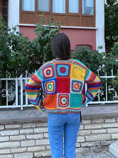 a woman wearing a colorful crocheted jacket standing on steps