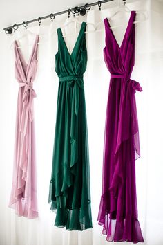 three different colored dresses hanging up on a rack in front of a white wall and curtain