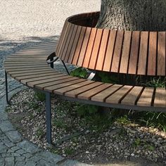 a wooden bench sitting next to a tree on top of a stone floored ground