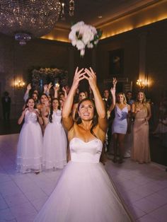 a woman in a white dress is holding her hands up to the sky while other people are