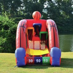 an inflatable basketball goalie bouncer on the grass near some trees and water