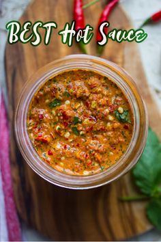 the best hot sauce recipe in a jar on a cutting board with peppers and basil