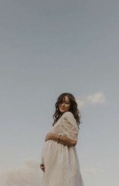 a woman in a white dress standing on top of a hill with her arms crossed