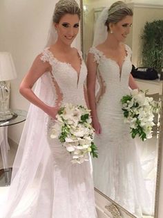 two women in wedding gowns standing next to each other and one is holding a bouquet