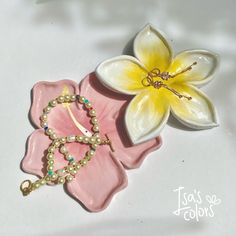 a pink flower and beaded bracelet laying on top of a white surface with a yellow flower in the middle