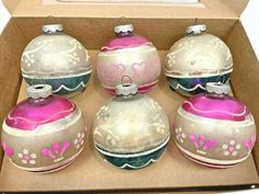 six ornaments in a cardboard box with pink and white designs