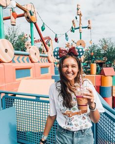 a woman standing in front of a carnival ride holding a drink and smiling at the camera