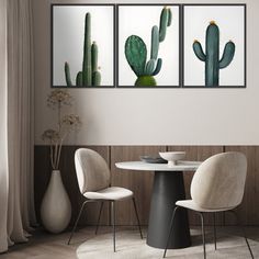 three cactus paintings hanging on the wall above a dining room table with two white chairs