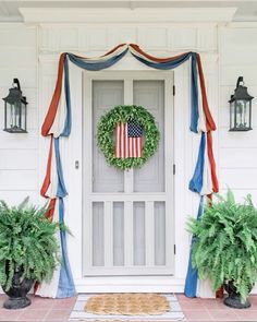 an american flag wreath hangs on the front door of a house with potted plants