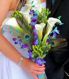 the bride and groom are holding their bouquets with peacock feathers on each one side