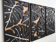 three black and white metal wall art panels with leaves on the sides, hanging on a wall