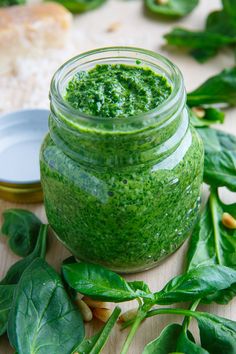 a jar filled with green pesto sitting on top of a wooden table next to spinach leaves