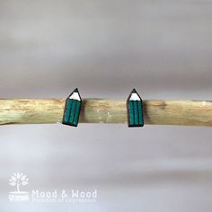 two small green earrings sitting on top of a wooden stick