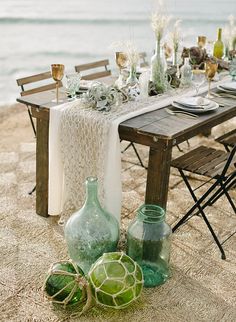 the table is set with green vases and place settings for an outdoor dinner on the beach