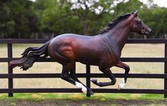 a statue of a running horse in a fenced - in area with grass and trees