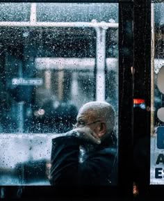 an old man sitting in front of a window on a rainy day with his hand to his face