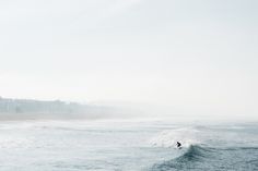 a person riding a surfboard on top of a wave in the ocean with buildings in the background