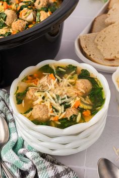 a bowl of soup with meatballs, spinach and carrots on the side