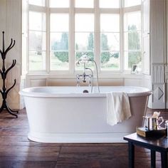 a white bath tub sitting next to a window in a room with wooden floors and walls