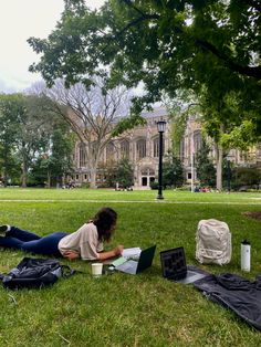 a woman laying on the grass working on her laptop