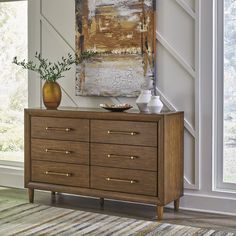 a dresser with two vases on top of it in front of a large painting