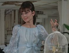 a woman standing next to a birdcage holding something in it's hand