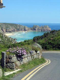 an empty road near the ocean with flowers growing out of it's cracks in the wall