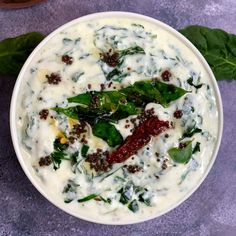 a white bowl filled with spinach, cheese and other toppings on top of a purple surface